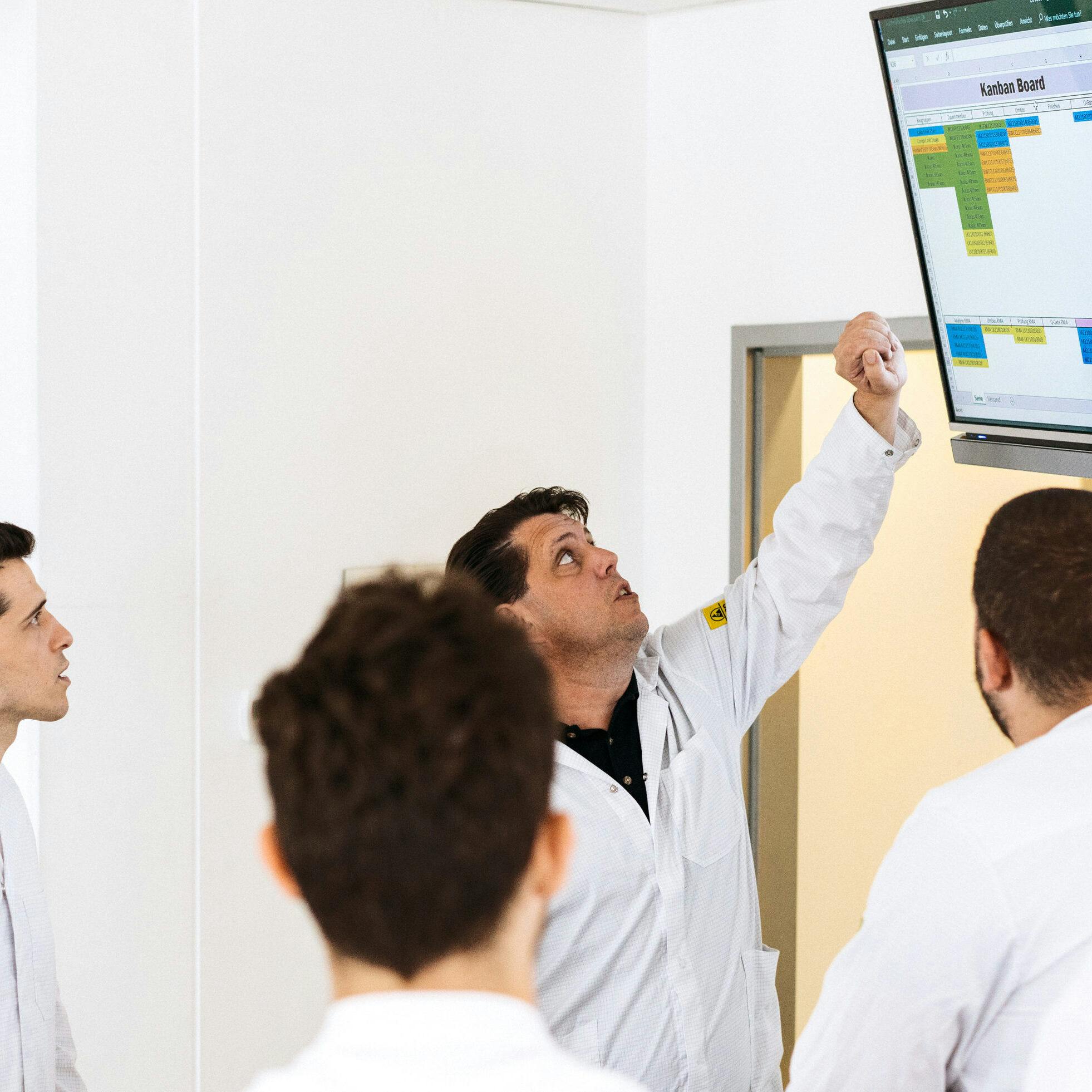Stand-up meeting in front of an electronic Kanban board